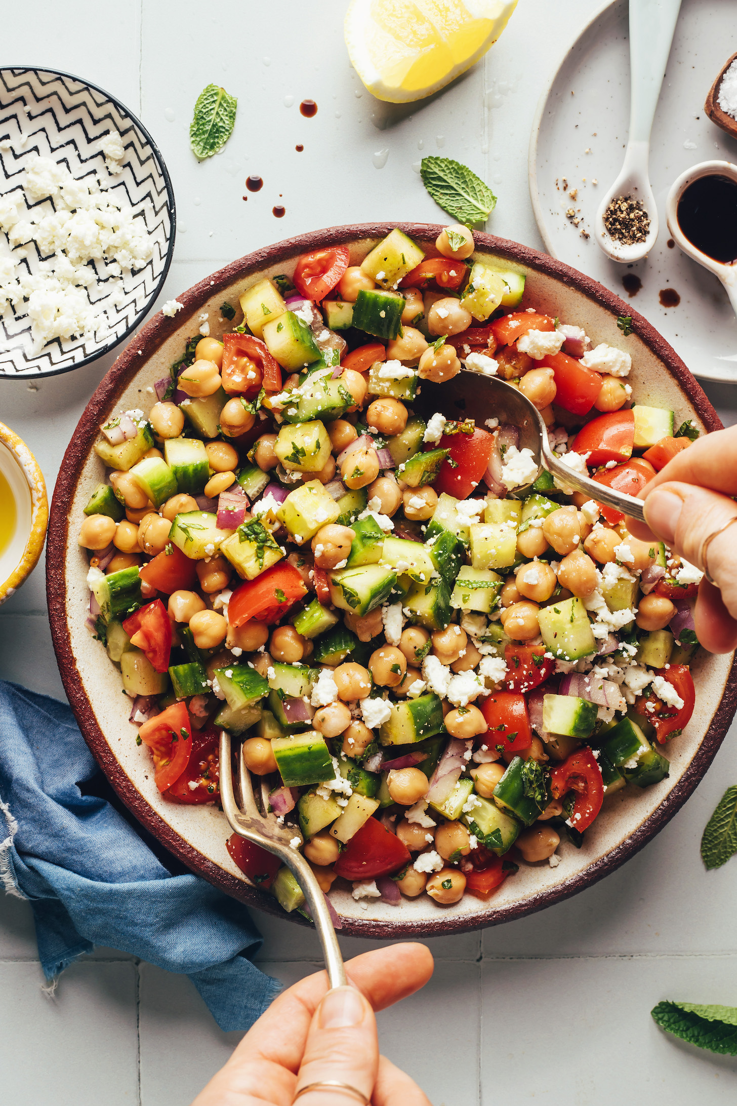 Using a fork and spoon to mix a bowl of Mediterranean cucumber tomato chickpea salad