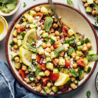 Bowl of our Mediterranean cucumber tomato chickpea salad with fresh mint leaves and lemon slices