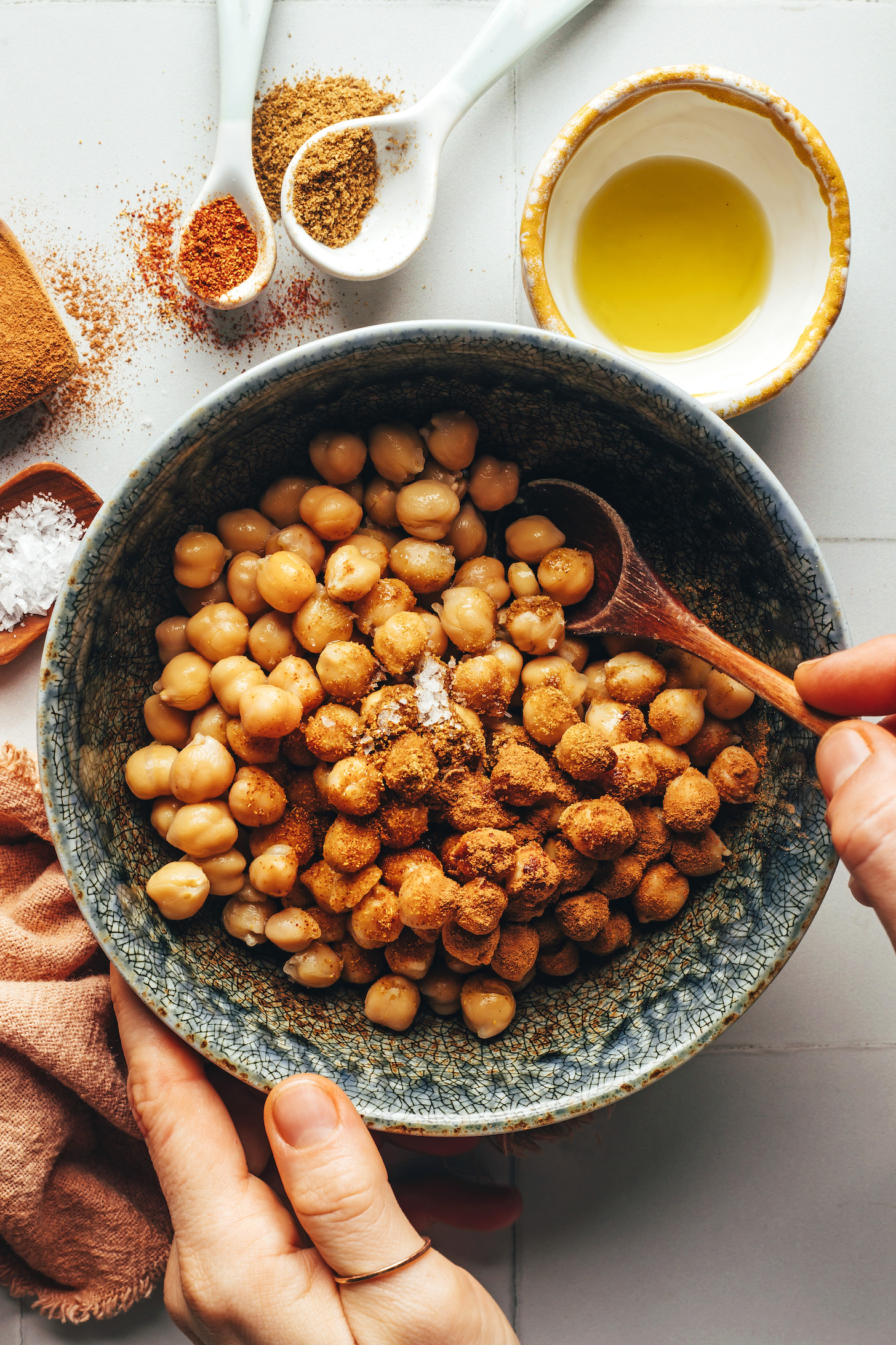 Using a spoon to mix chickpeas in a bowl with spices and salt