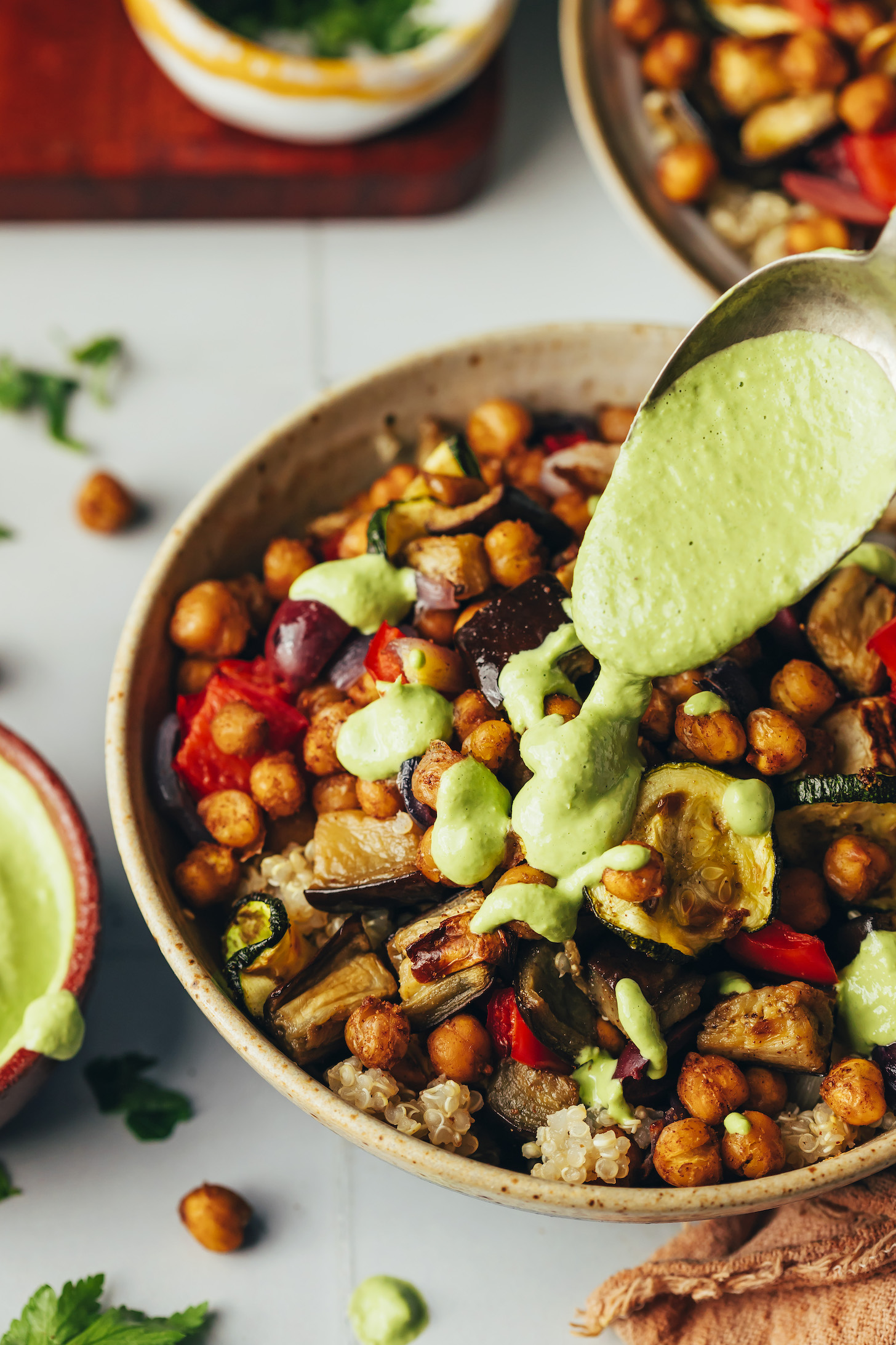 Drizzling green tahini sauce onto a bowl of roasted veggies, chickpeas, and quinoa