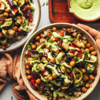 Hands holding the sides of a bowl of roasted chickpeas, quinoa, and veggies topped with green tahini sauce