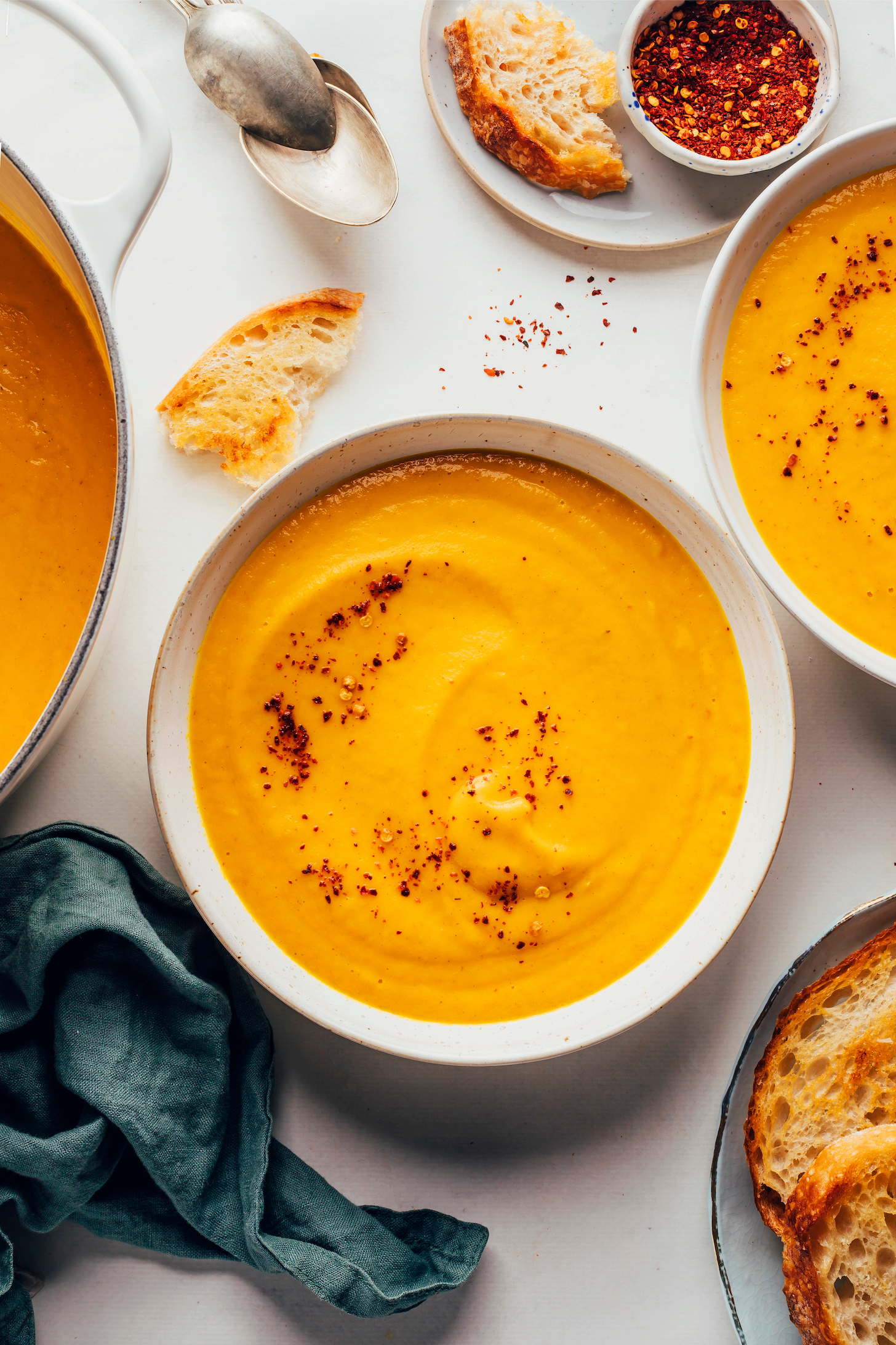 Large pot and bowls of creamy carrot soup next to slices of toasted bread