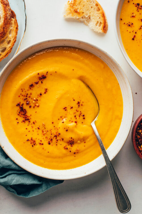 Close up shot of a bowl of creamy vegan carrot soup topped with red pepper flakes