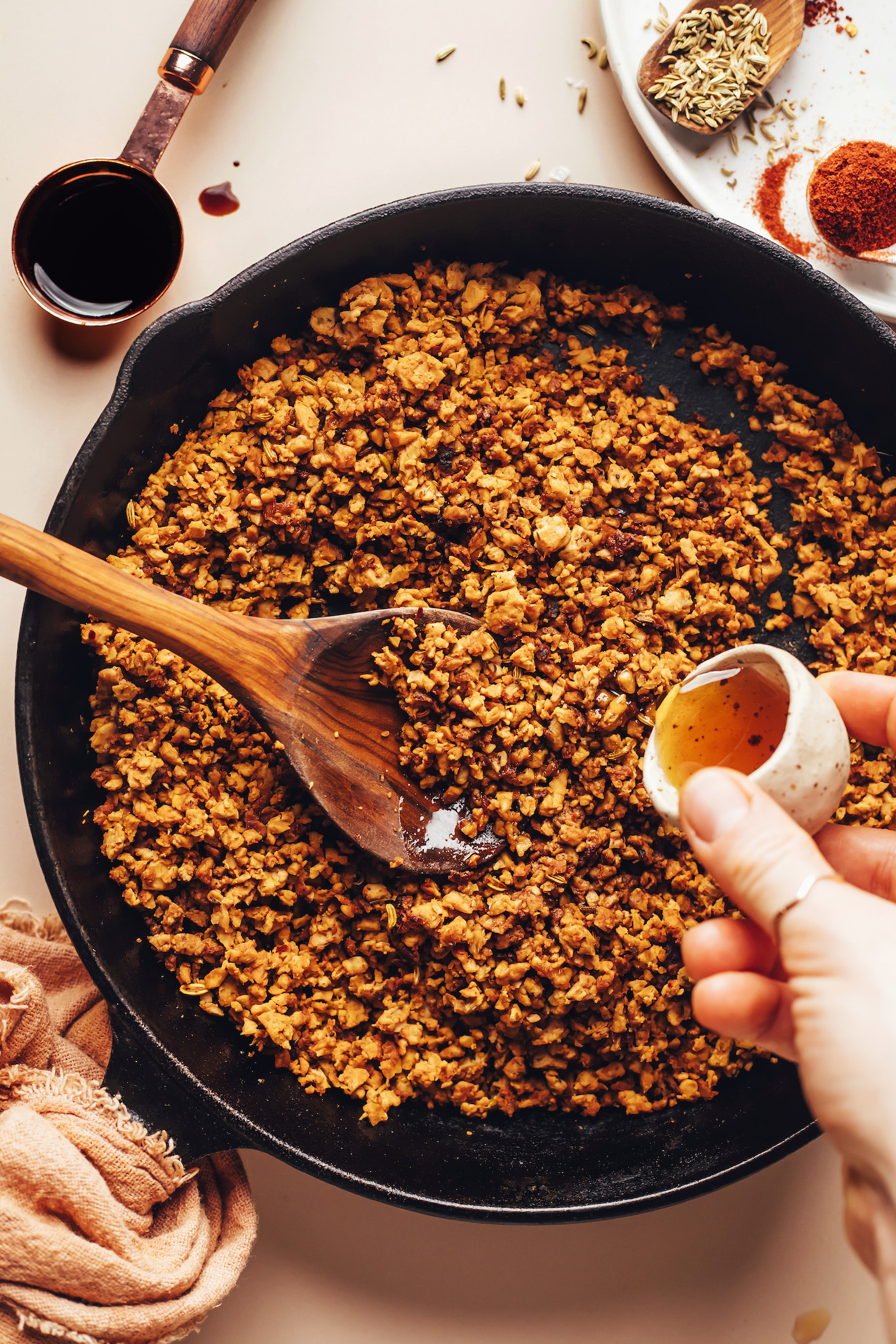 Pouring maple into a skillet of seasoned crumbled tempeh