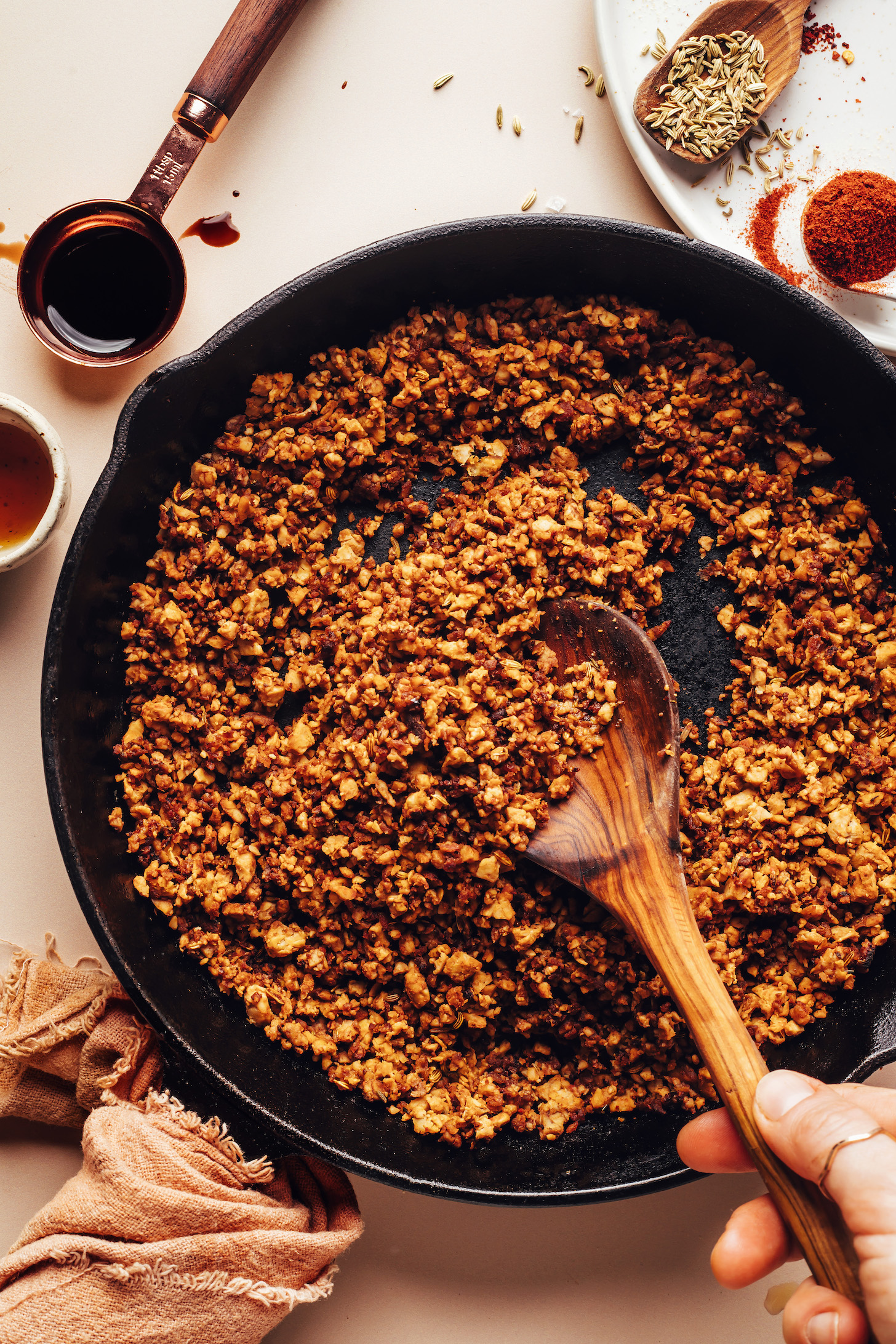 Wooden spoon stirring vegan tempeh sausage crumbles in a cast iron skillet