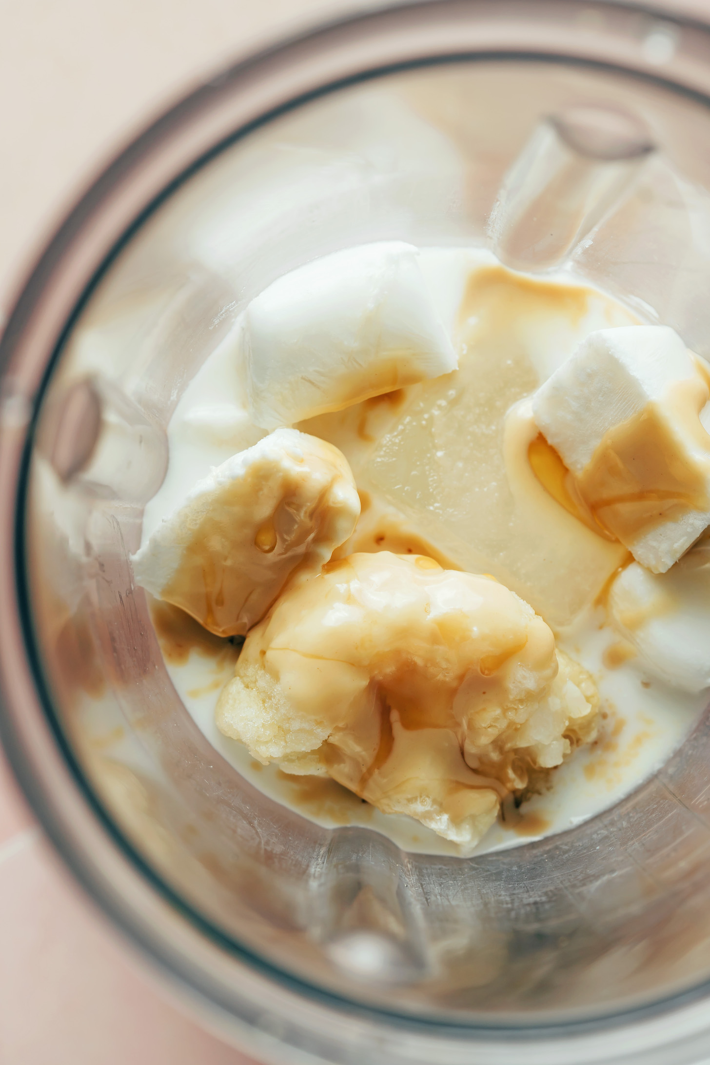 Blender with dairy-free milk, coconut milk ice cubes, frozen cauliflower, tahini, maple syrup, and vanilla