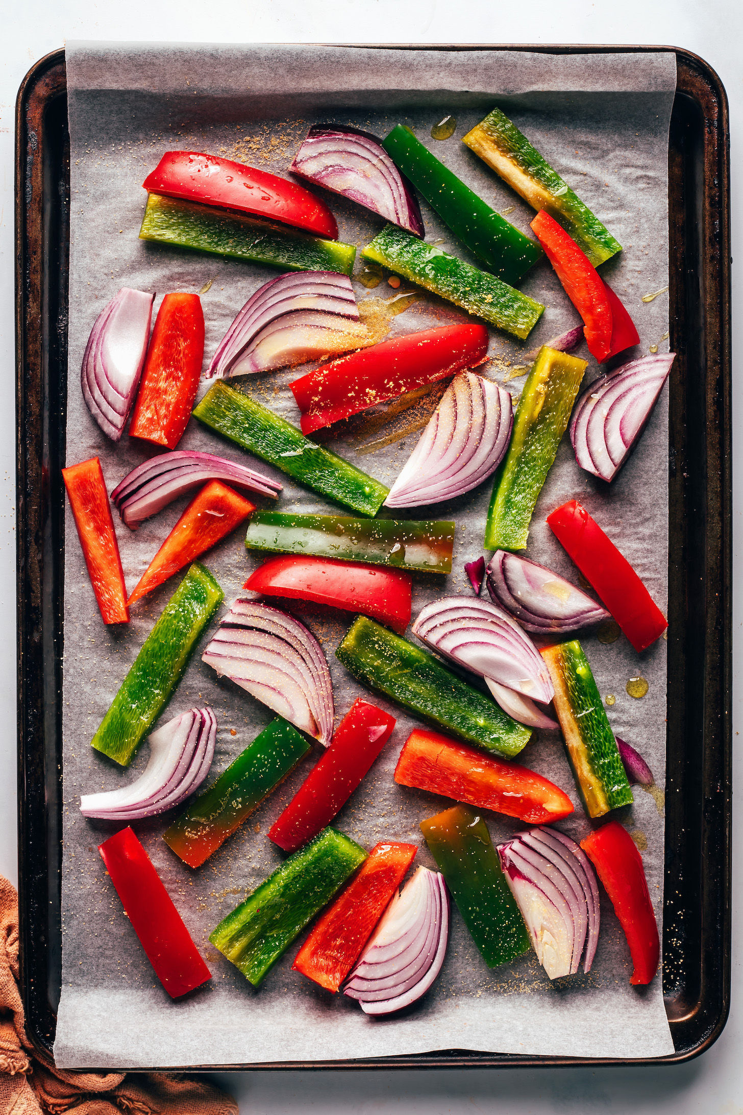 Sliced peppers and onions on a parchment-lined baking sheet