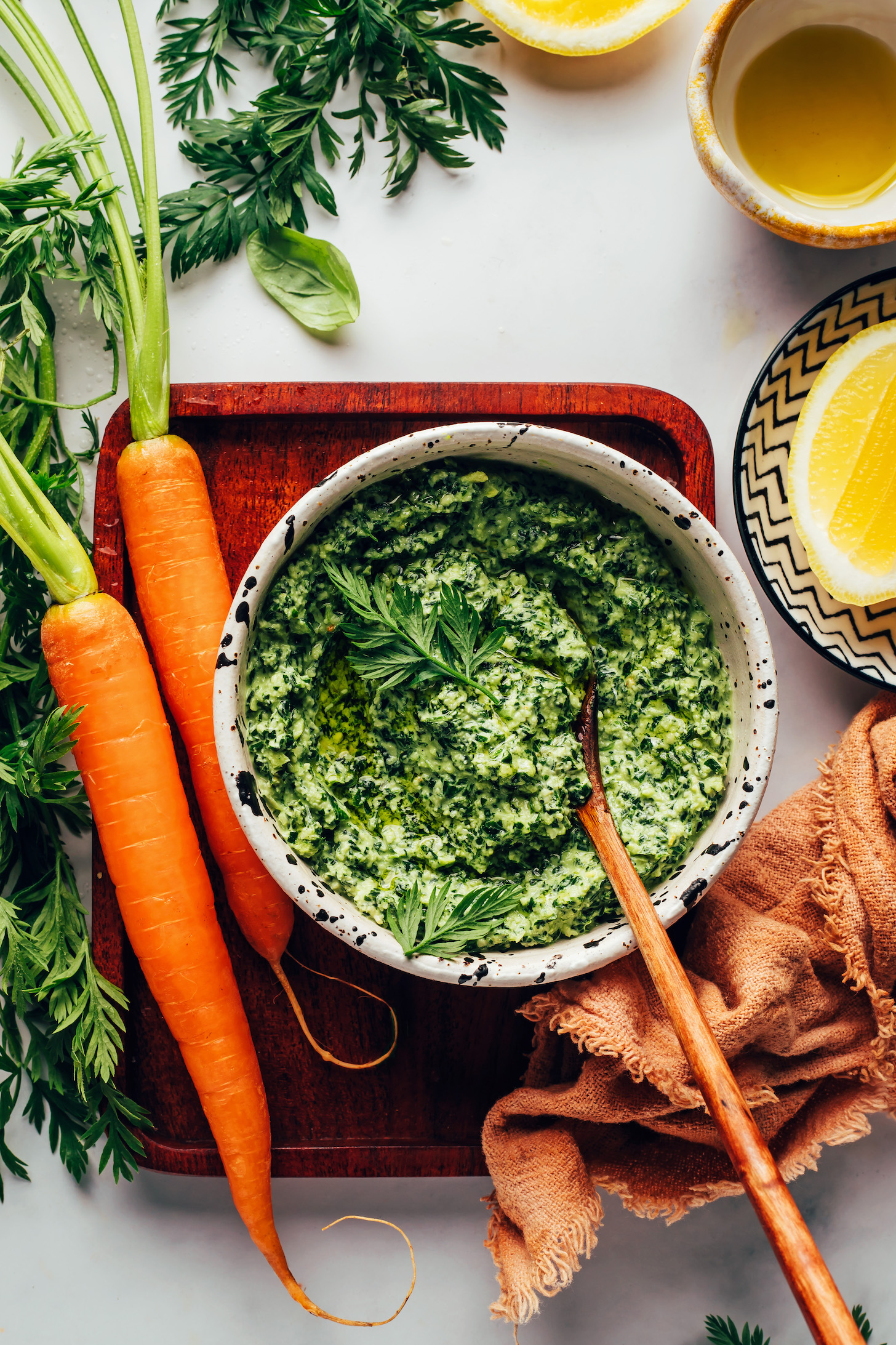 Lemons, olive oil, carrots with tops, and a bowl of carrot top pesto