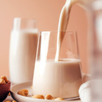 Pouring homemade cashew milk from a pitcher into a glass