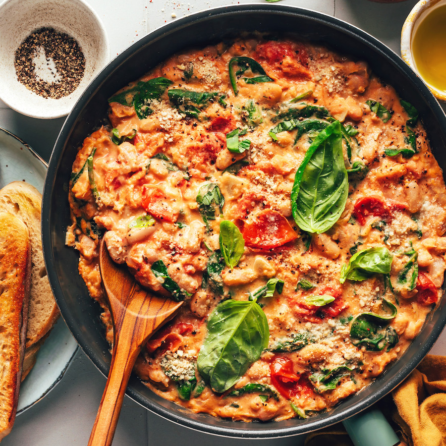 Creamy vegan skillet meal with white beans, burst cherry tomatoes, spinach, and fresh basil