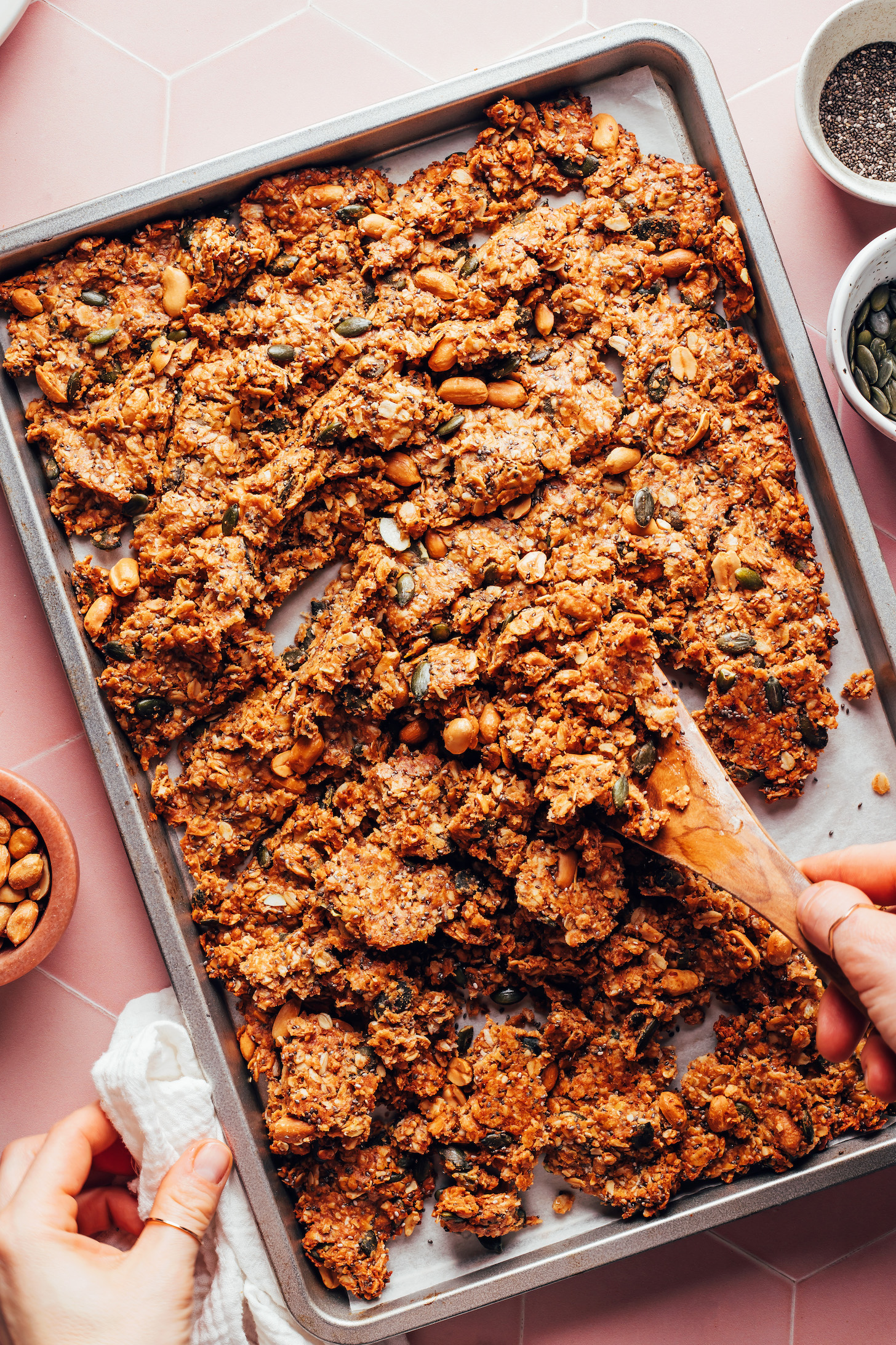 Breaking up peanut butter cookie granola into chunks on a baking sheet