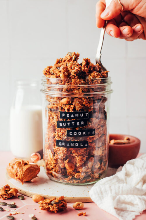 Spoon dipping into a jar of peanut butter cookie granola