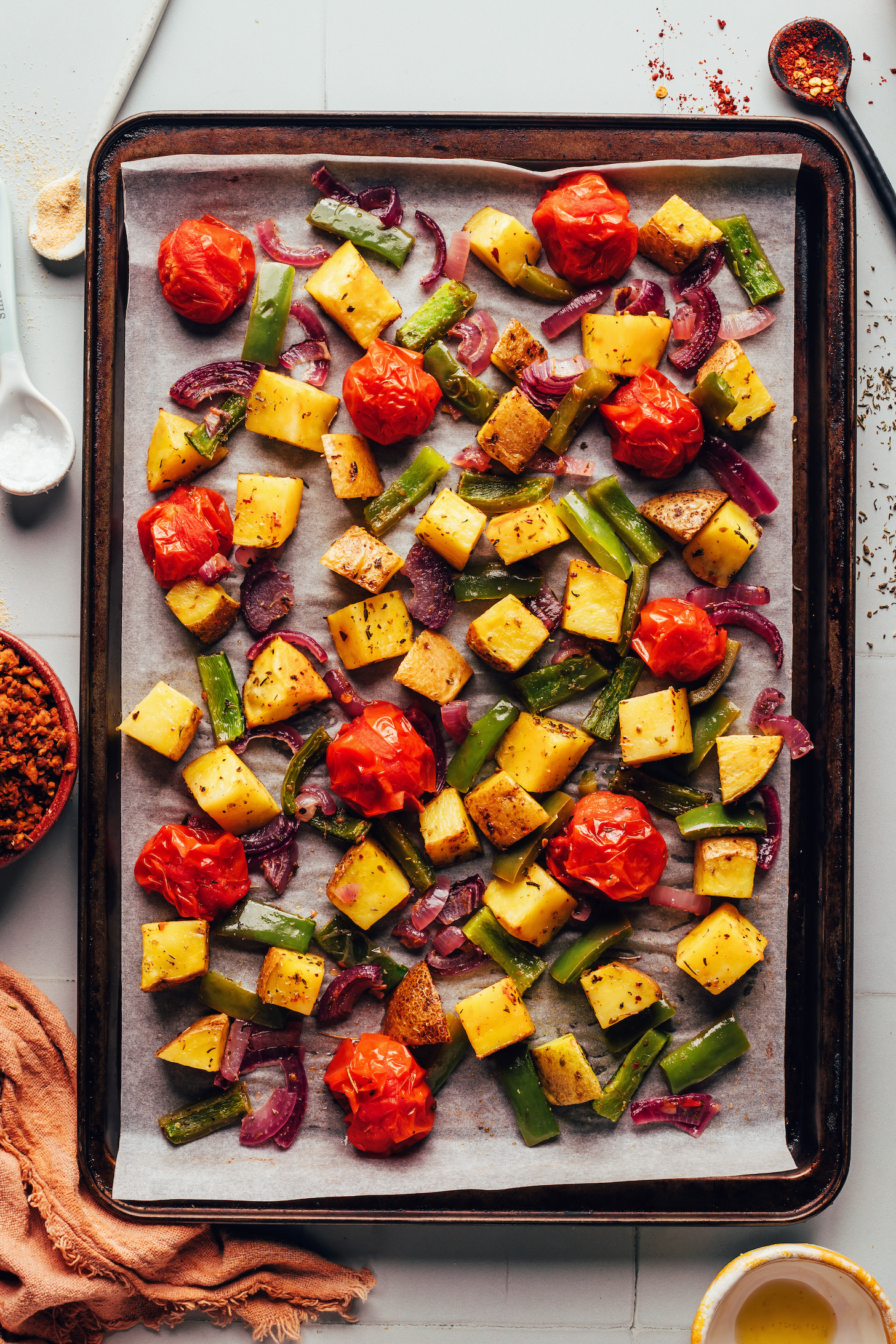 Baking sheet with roasted potatoes, red onion, green bell pepper, and cherry tomatoes