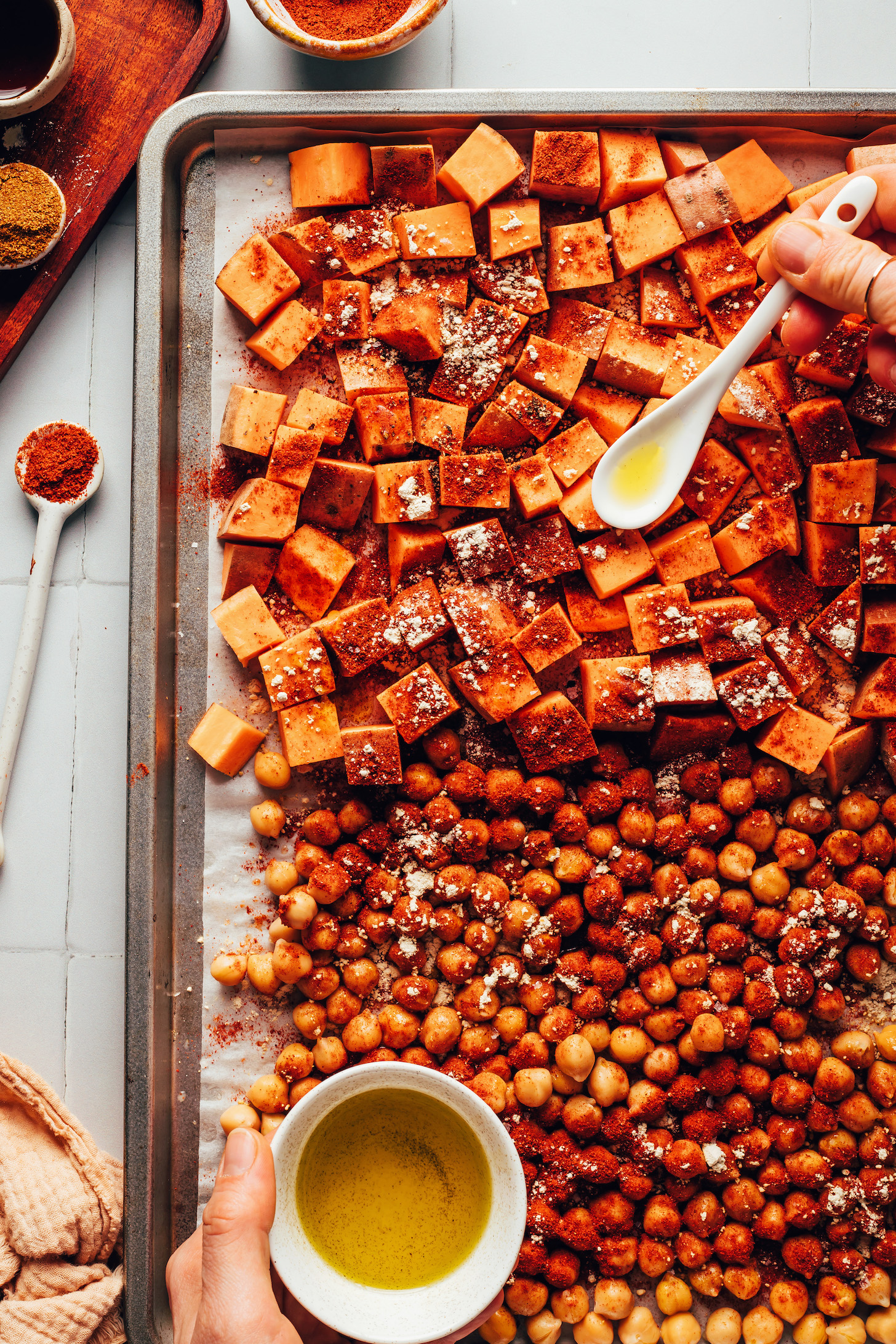 Drizzling oil onto a baking sheet of chickpeas and cubed sweet potatoes