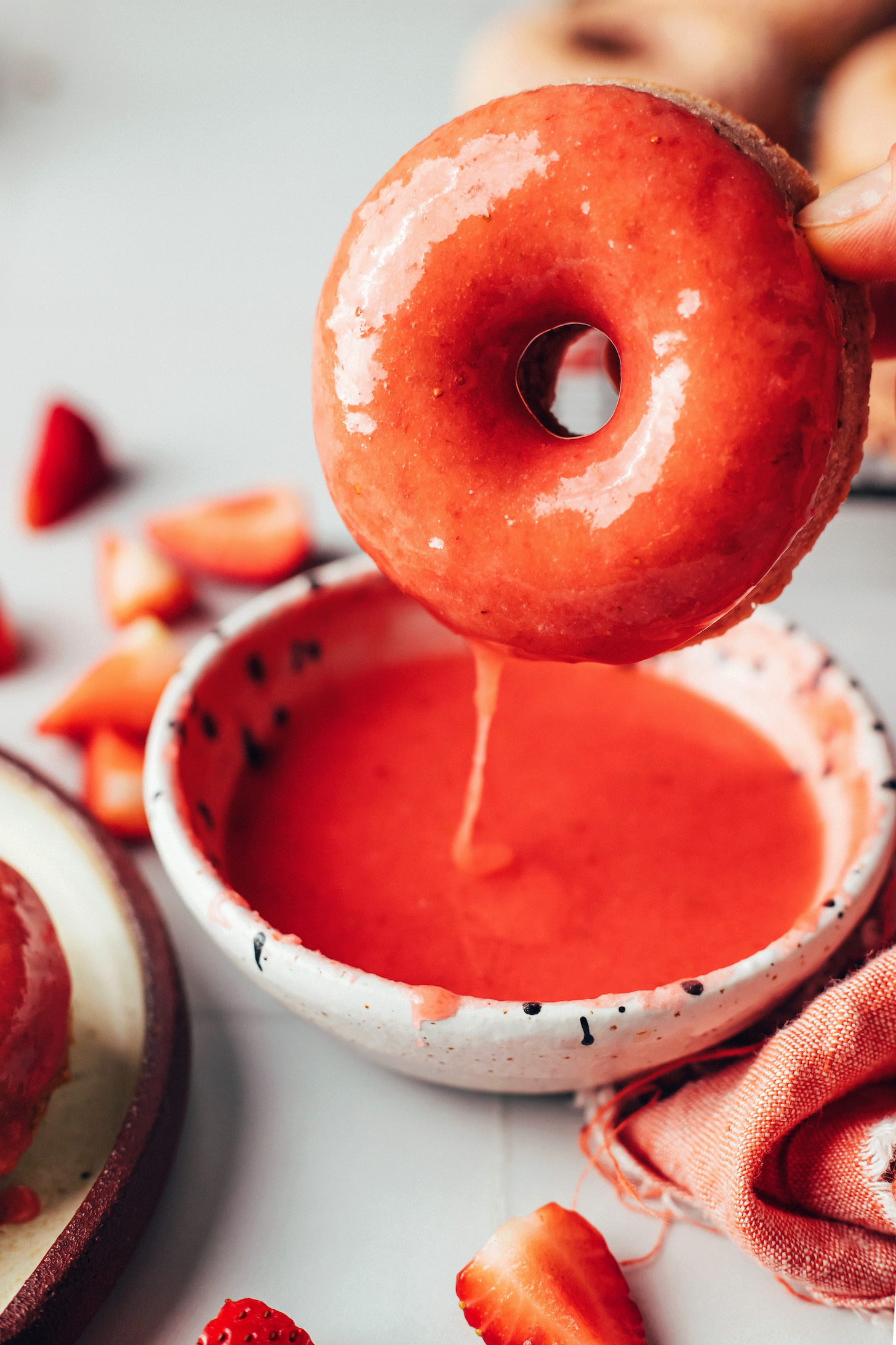 Dipping a strawberry donut into a vibrant pink strawberry glaze