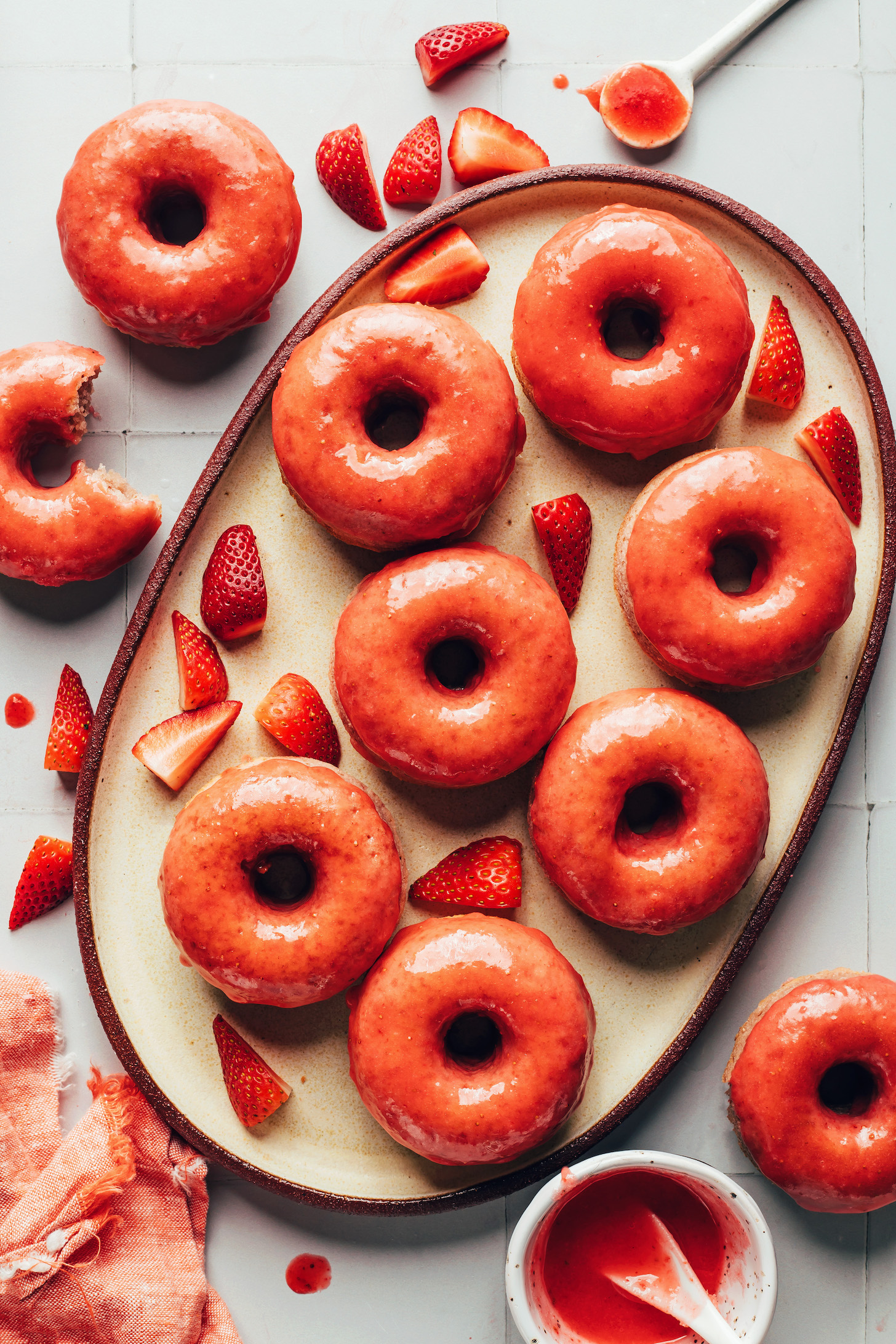 Platter of baked vegan gluten-free strawberry donuts surrounded by fresh strawberries