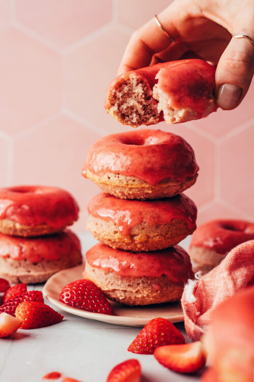 Holding a partially eaten baked strawberry donut over a stack of more donuts