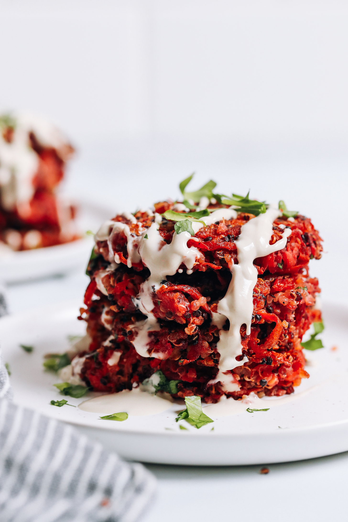 Stack of quinoa root vegetable fritters garnished with tahini sauce and parsley