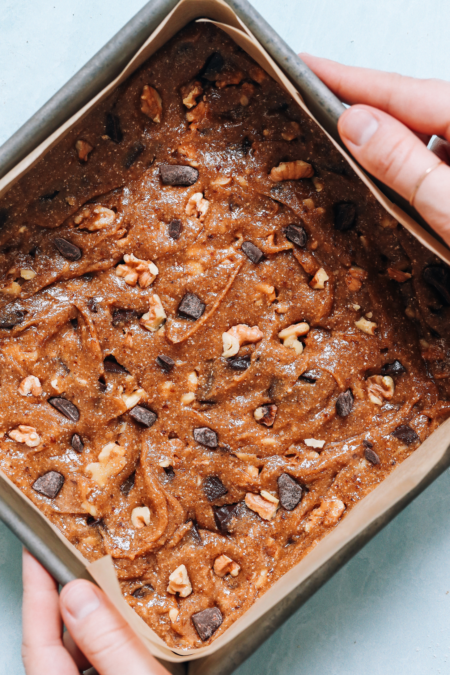 Chocolate chip cookie bar batter in a parchment-lined baking pan