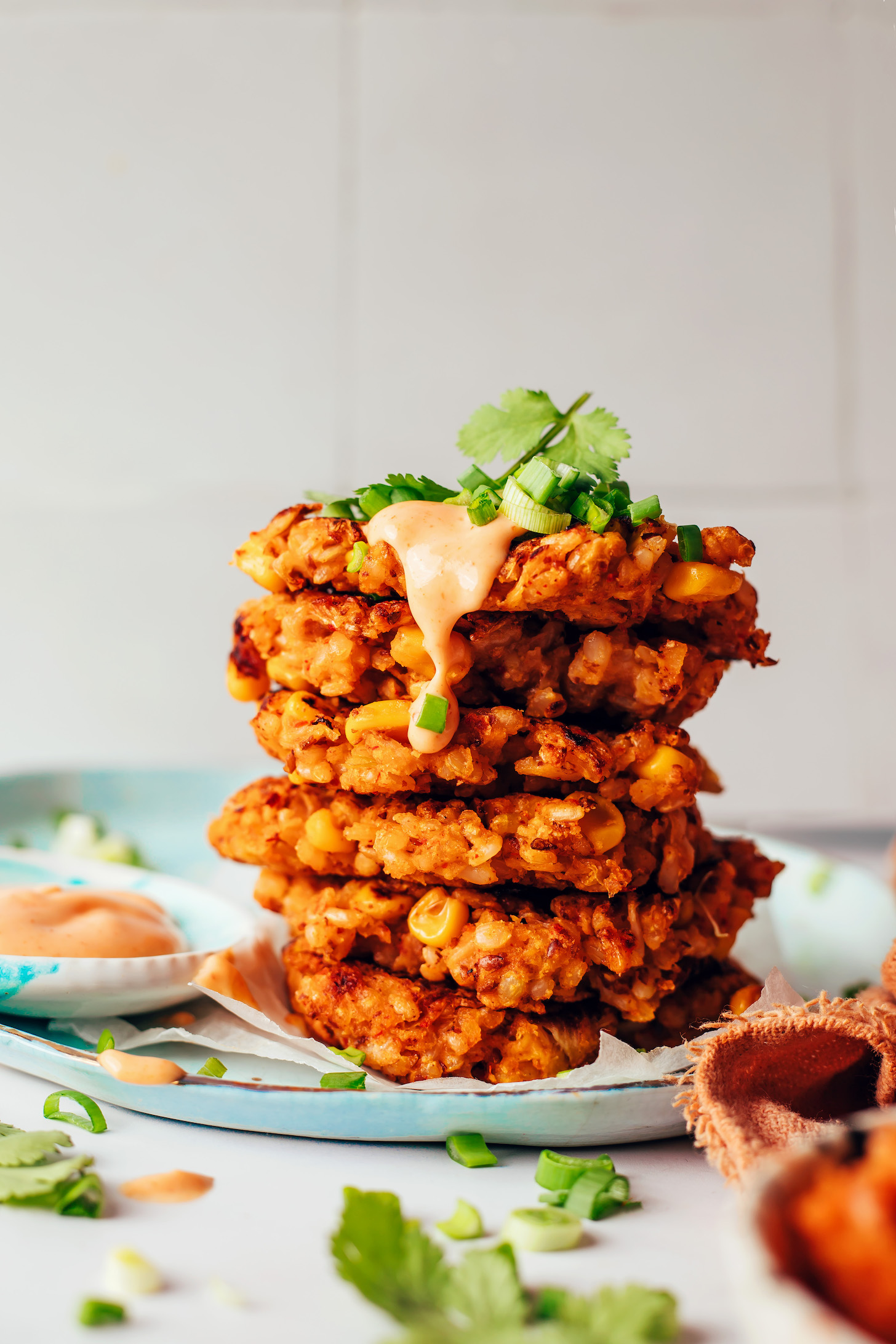 Stack of kimchi rice fritters topped with sriracha sour cream, green onions, and cilantro