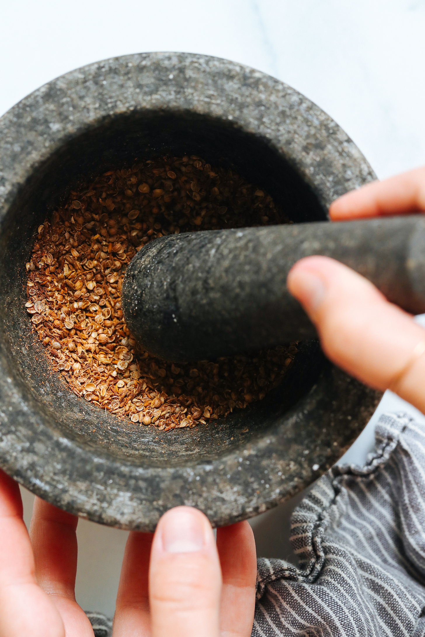 Using a mortar and pestle to grind cumin seeds and coriander seeds