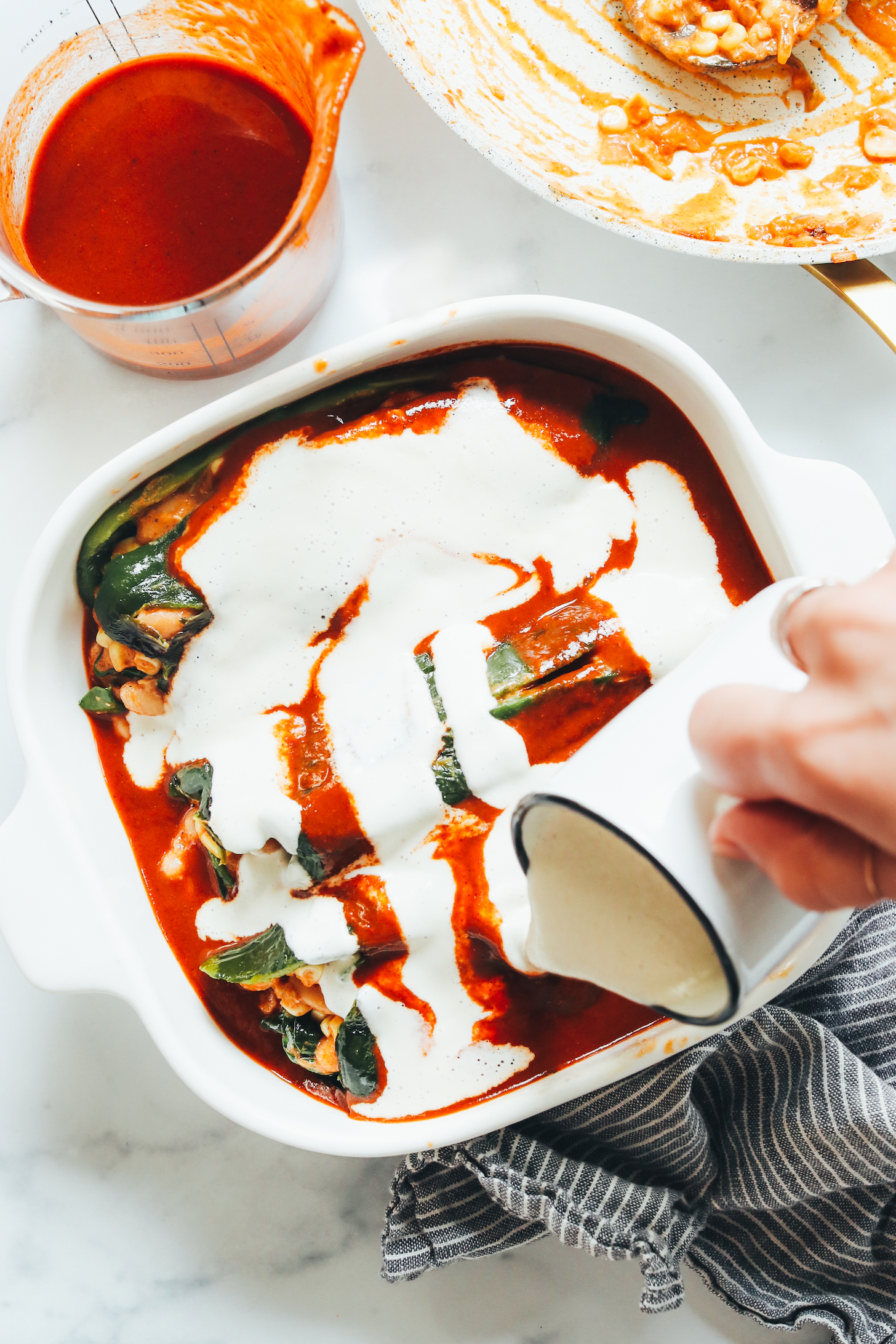 Drizzling cashew cream sauce over a pan of baked chile rellenos