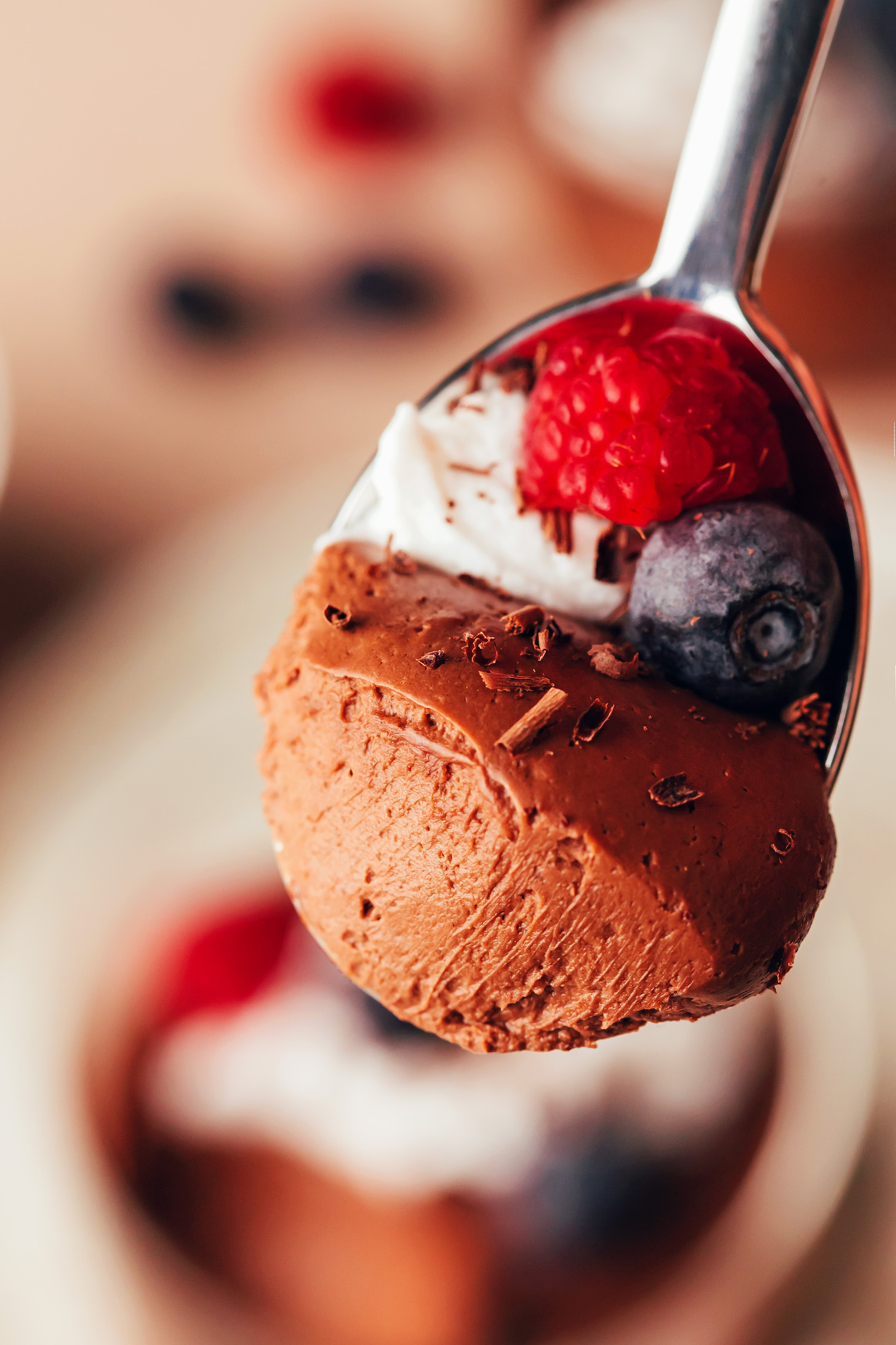 Close up shot of a spoon with a bite of chocolate pot de creme, coconut whipped cream, and berries