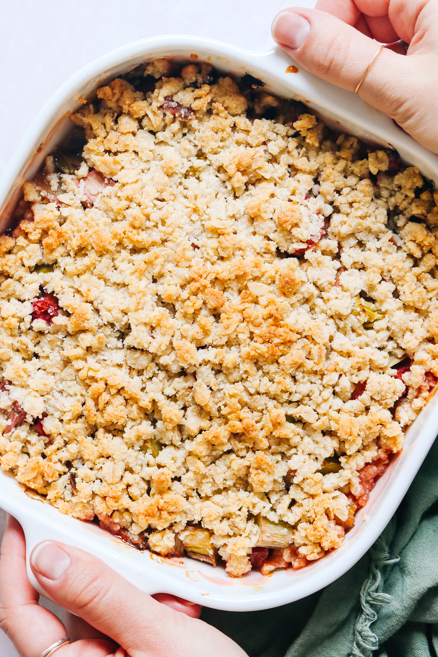 Hands holding the sides of a baking dish filled with vegan gluten-free rhubarb crisp