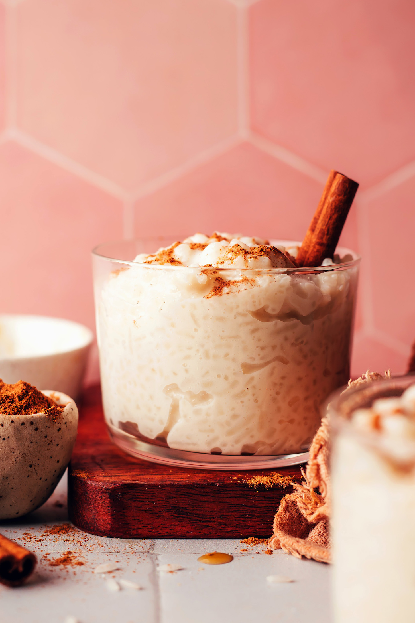 Small dessert glass filled with vegan rice pudding and garnished with ground cinnamon and a cinnamon stick