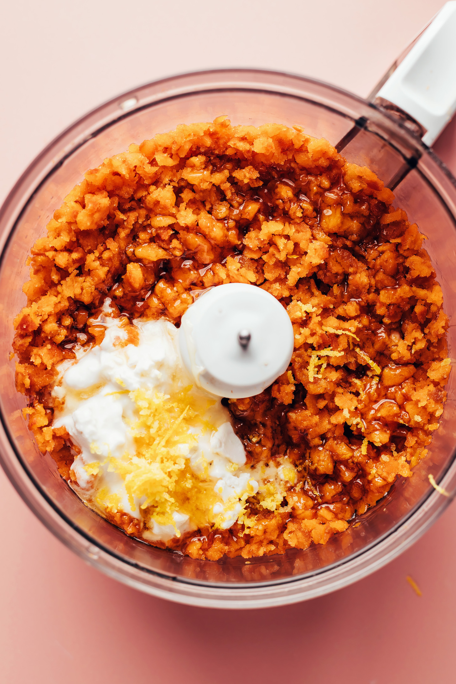 Food processor with bits of frozen apricot with agave, coconut cream, and lemon zest