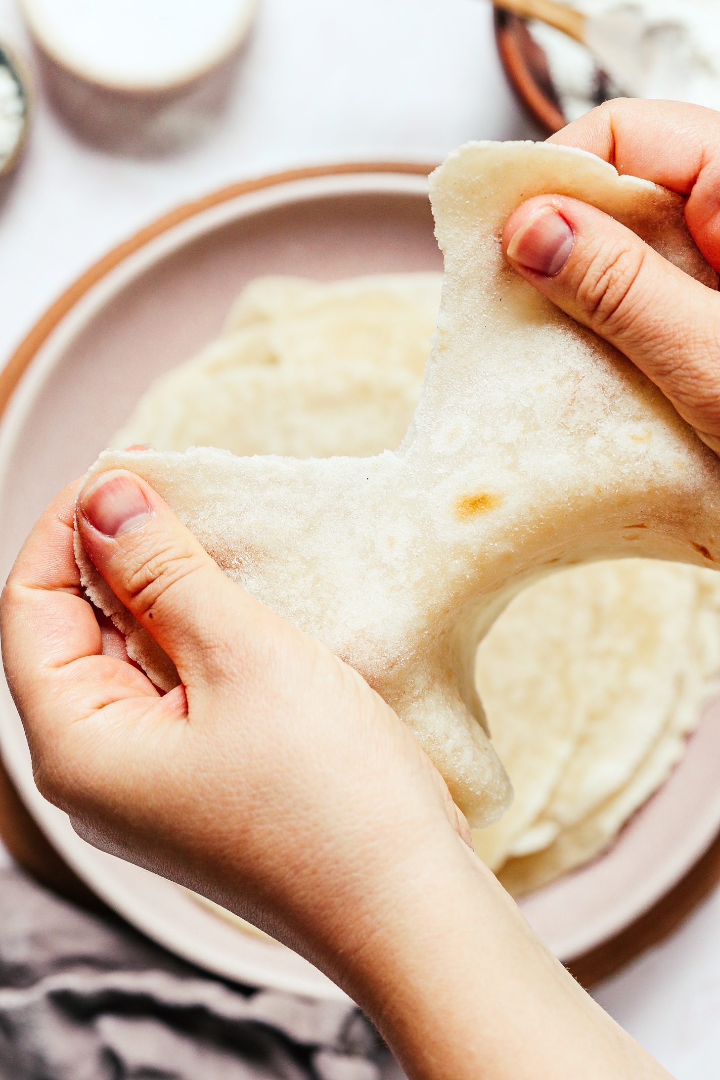Tearing a grain-free cassava flour tortilla between hands to show the chewy texture