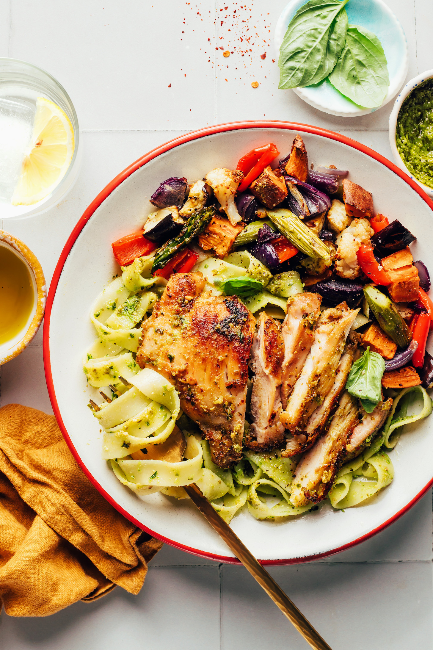Pesto pasta swirled on a fork next to a pesto chicken thigh and roasted vegetables