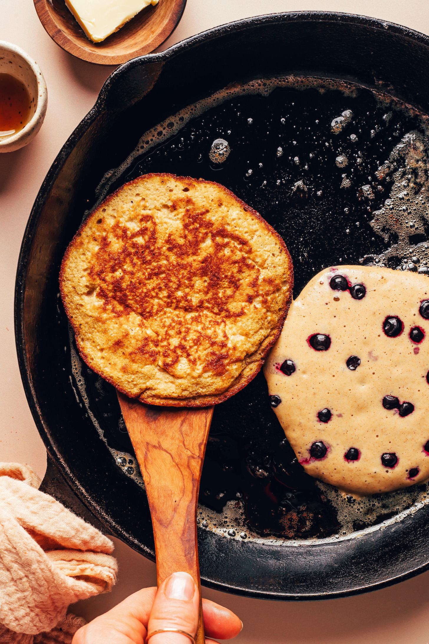 Two plantain pancakes cooking in a cast iron skillet