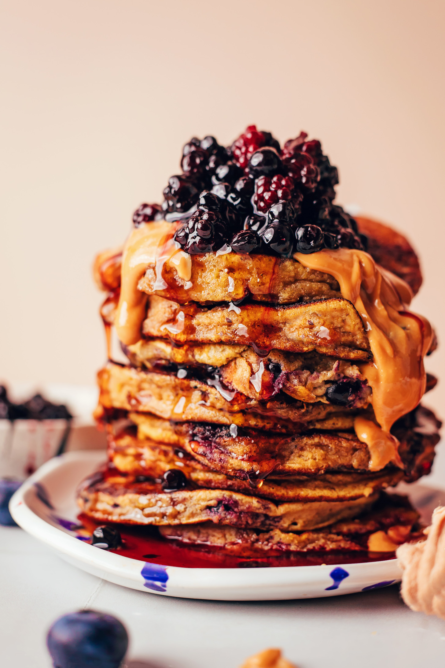 Stack of grain-free plantain pancakes topped with peanut butter, berry compote, and maple syrup