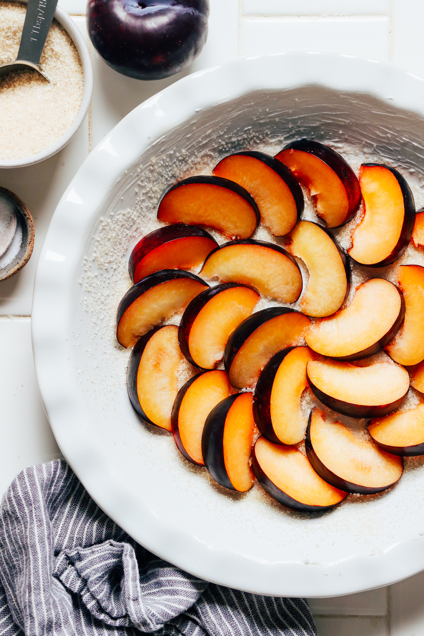 Sliced plums arranged in a circular pattern in a pie pan