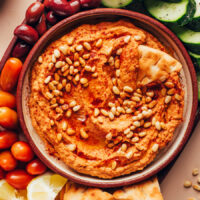 Overhead shot of a bowl of sun-dried tomato hummus on a platter with veggies and pita for dipping