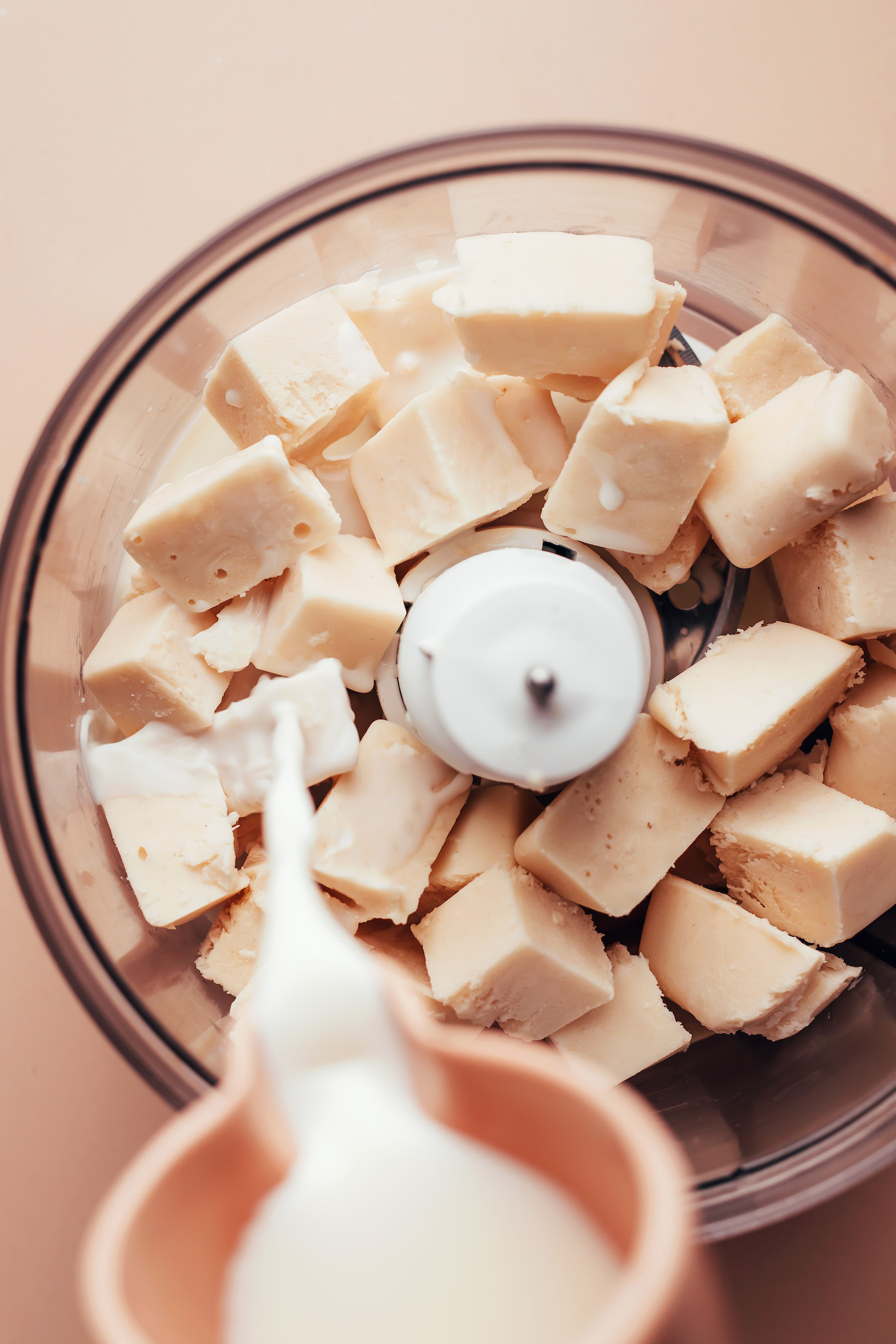 Adding almond milk to a food processor with vanilla coconut ice cubes