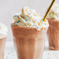Glasses filled with our vegan chocolate milkshake and topped with dairy-free whipped cream and sprinkles
