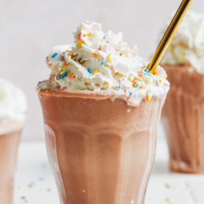 Glasses filled with our vegan chocolate milkshake and topped with dairy-free whipped cream and sprinkles