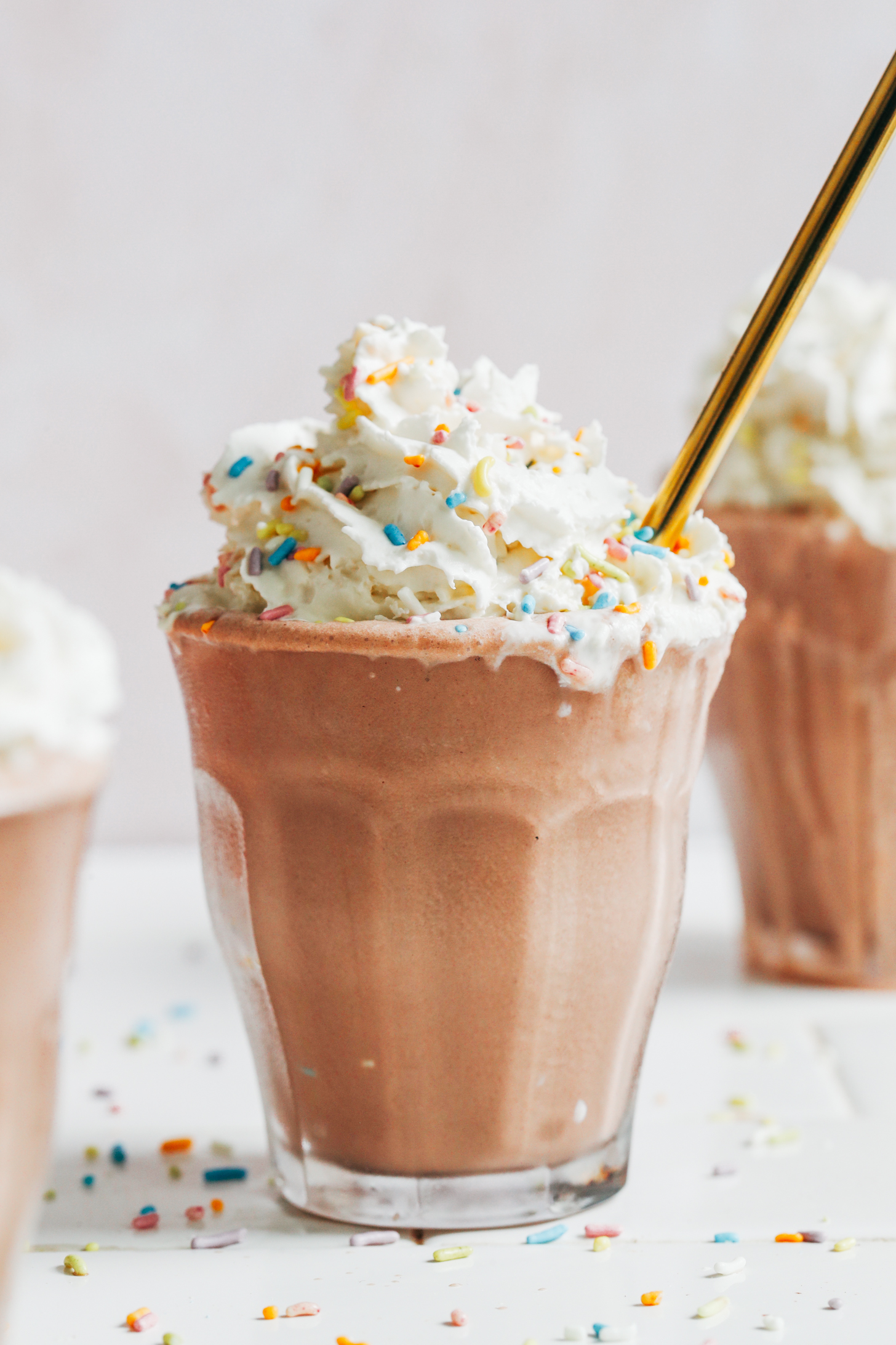 Glass of our thick and creamy vegan chocolate milkshake topped with dairy-free whipped cream and sprinkles