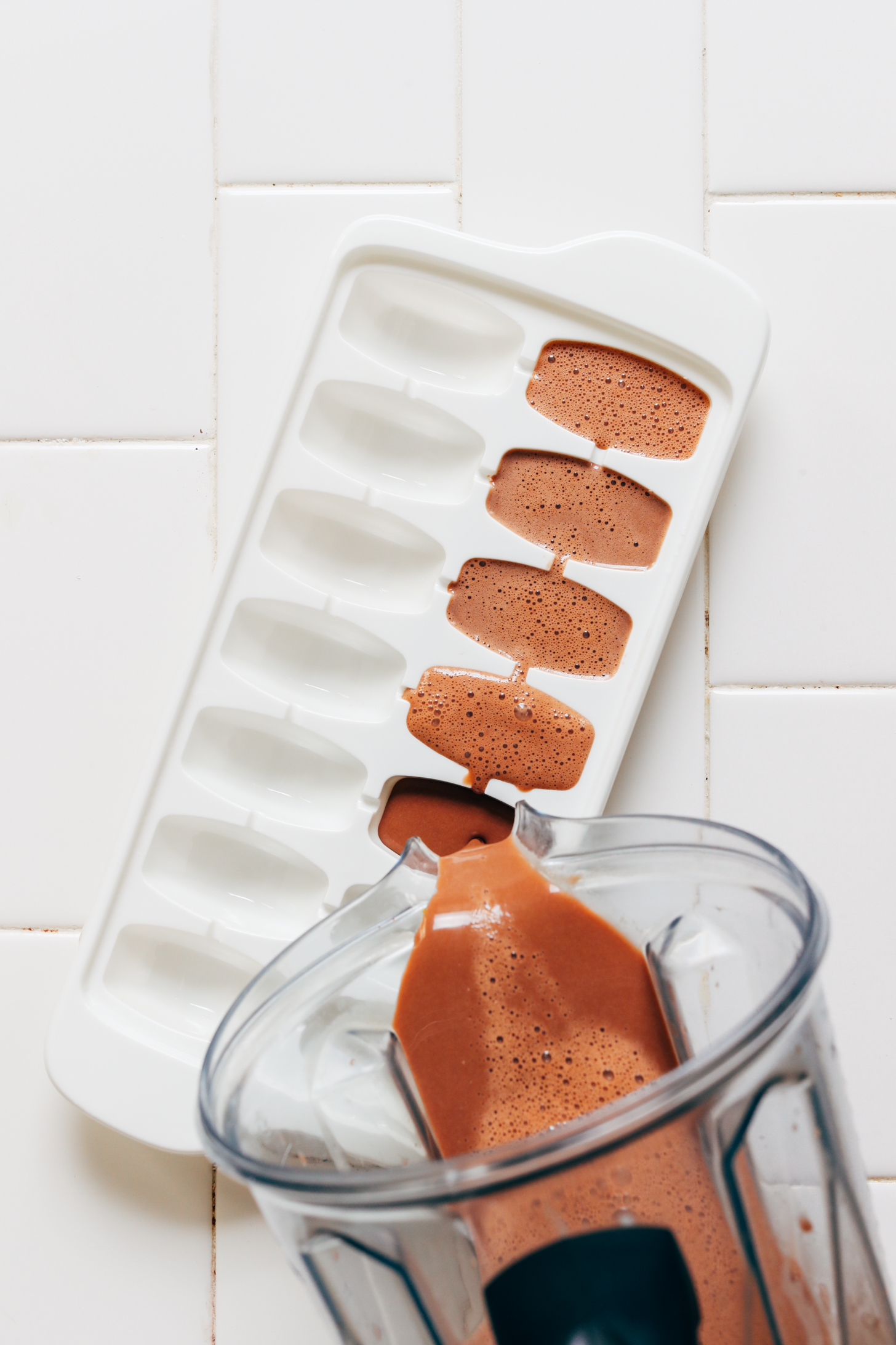 Pouring chocolate coconut milk from a blender into an ice cube tray