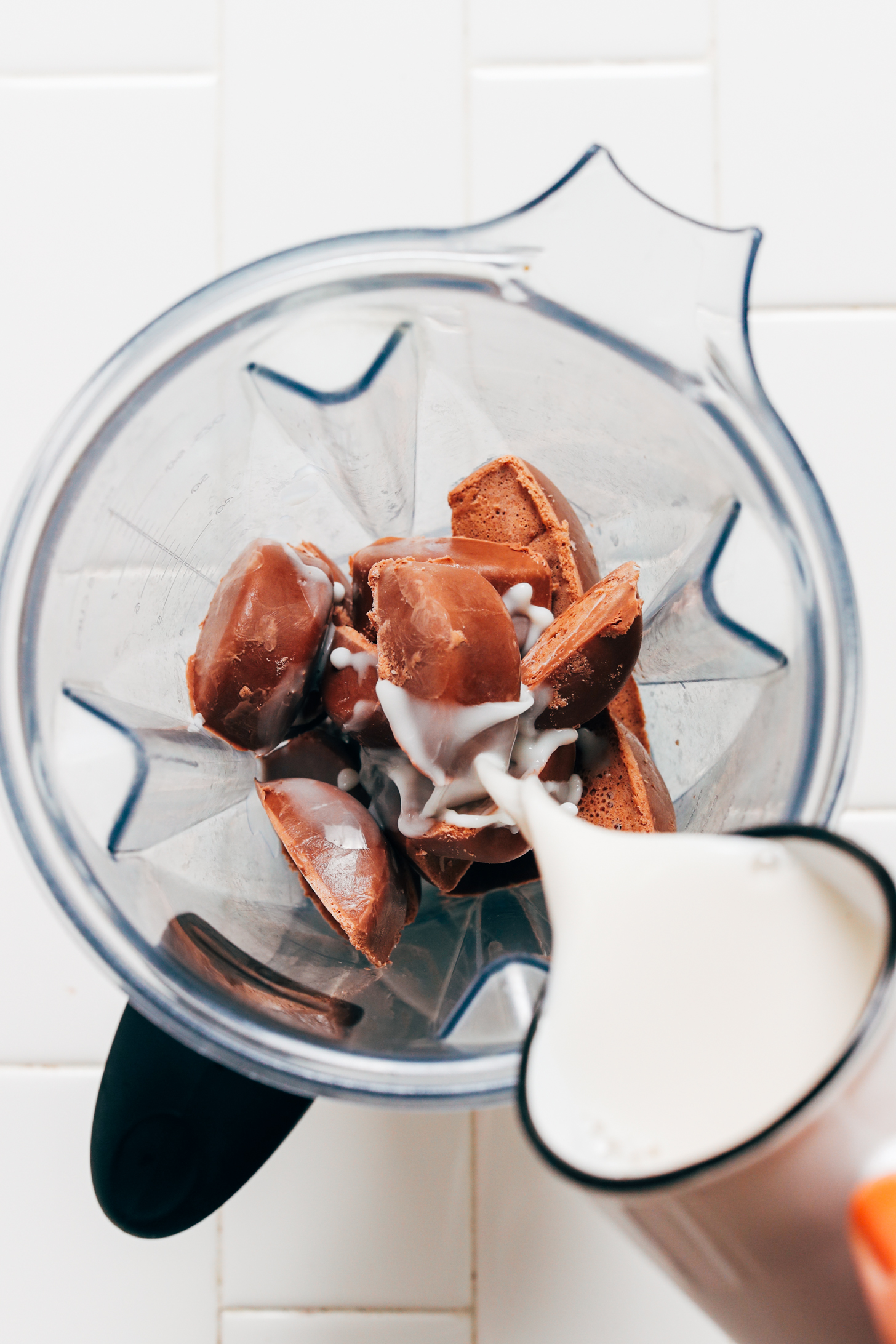 Pouring almond milk over chocolate milk ice cubes in a Vitamix blender