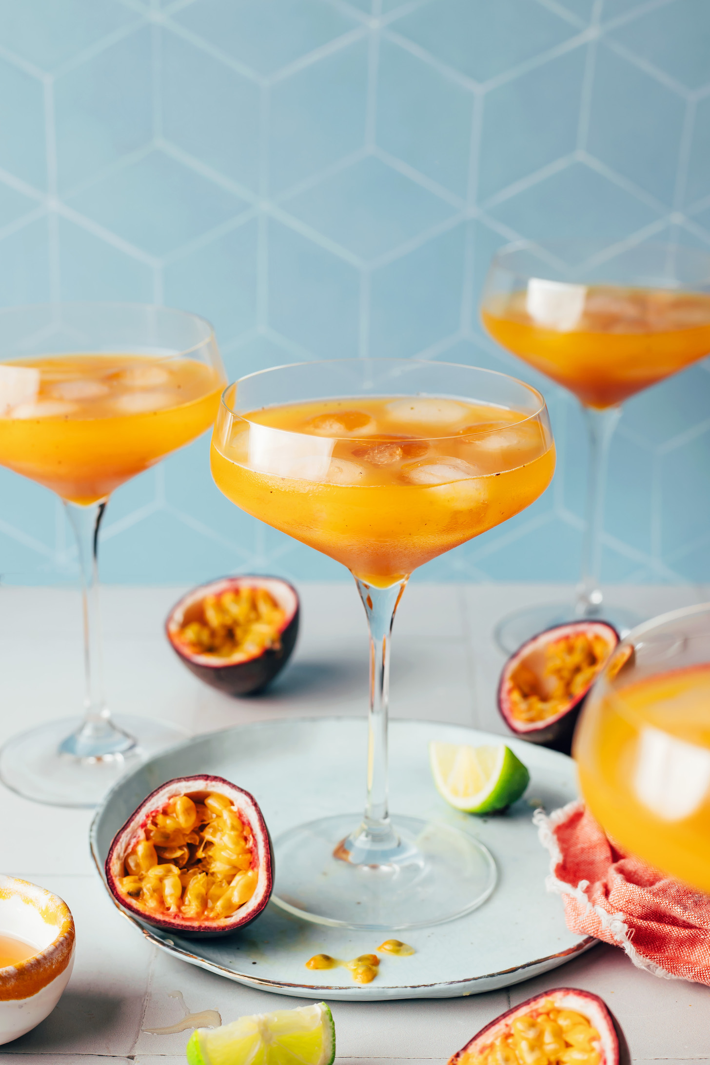 Three glasses of iced passion fruit mocktails with fresh passion fruit halves and lime wedges next to them