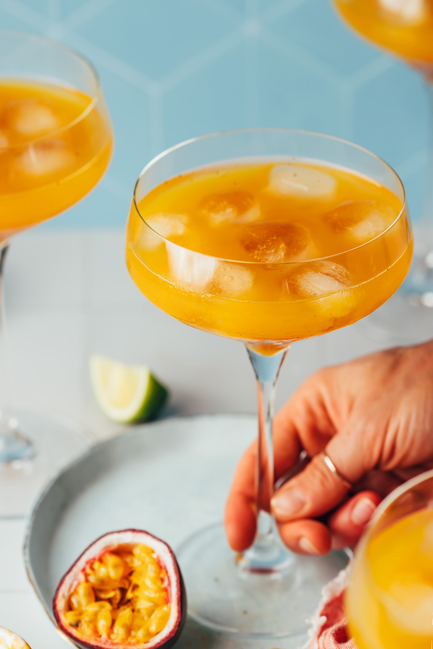 Hand reaching in to pick up a stemmed glass of our passion fruit mocktail recipe