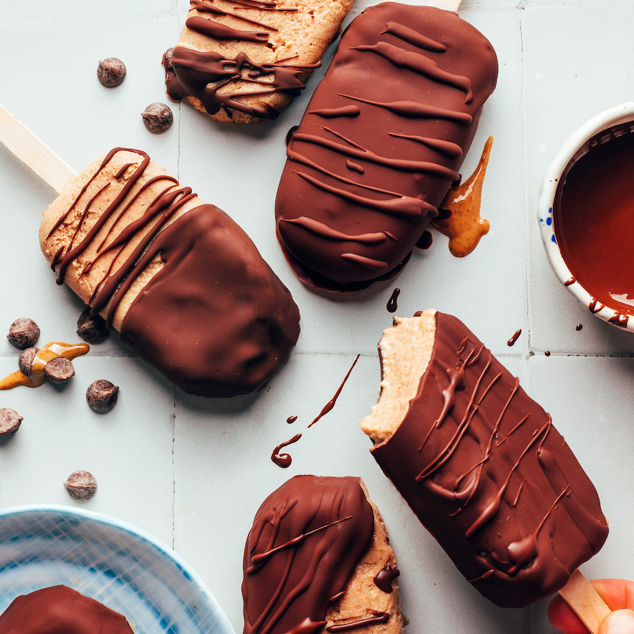 Five vegan chocolate peanut butter ice cream bars with chocolate chips and a bowl of melted chocolate