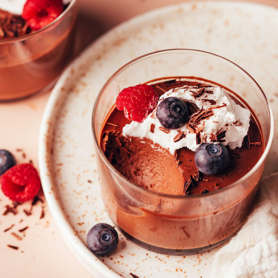 Small glass of vegan chocolate pot de creme topped with coconut whipped cream and berries