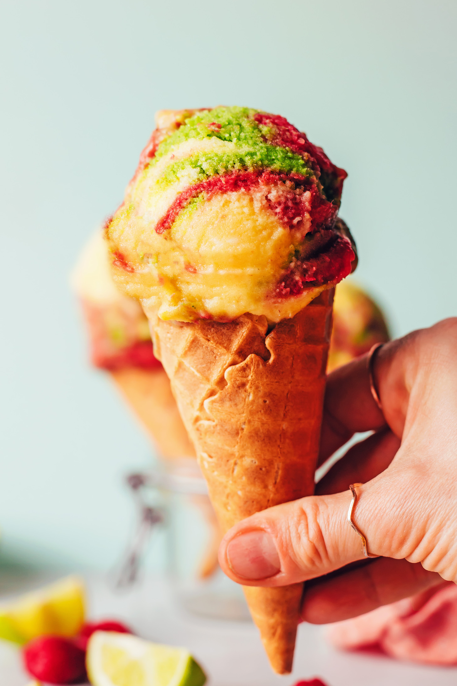 Hand holding an ice cream cone with homemade vegan rainbow sherbet ice cream