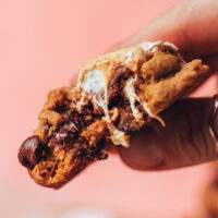 Holding a partially eaten s'mores cookies that shows the gooey marshmallows and melty chocolate