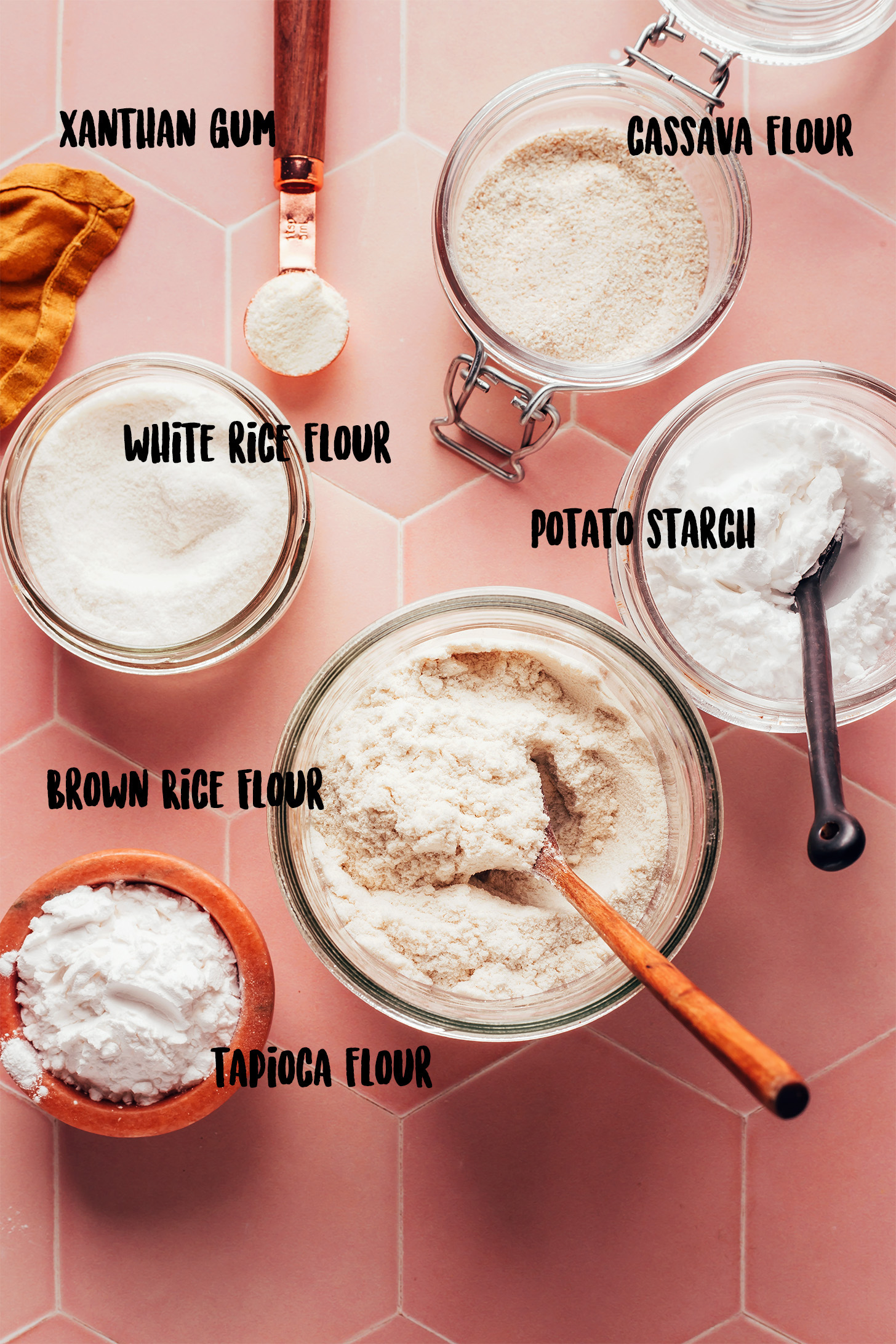 Jars, bowls, and spoonfuls of xanthan gum, white rice flour, brown rice flour, tapioca starch, potato starch, and cassava flour