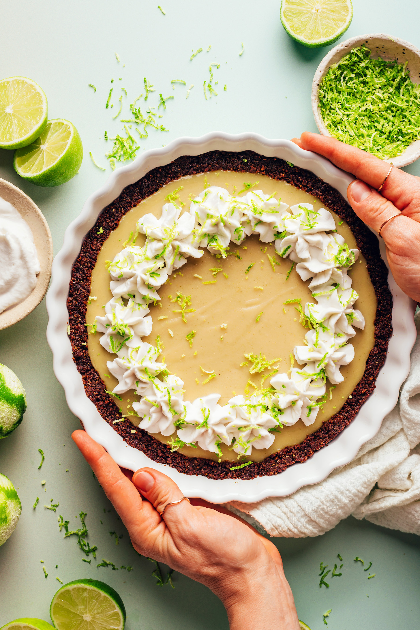 Hands holding the sides of a pie pan filled with a vegan key lime pie with a gluten-free graham cracker crust